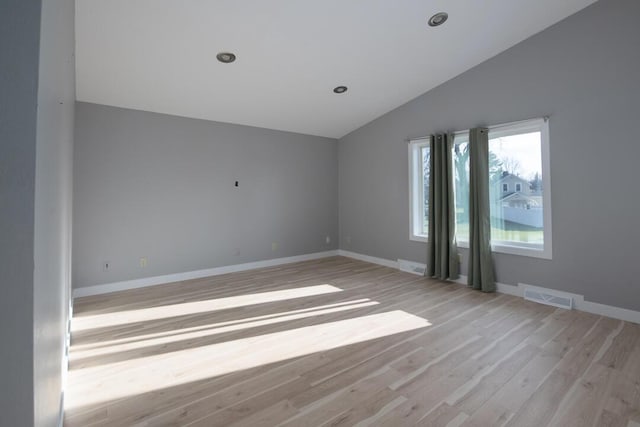 spare room with visible vents, baseboards, vaulted ceiling, and light wood finished floors