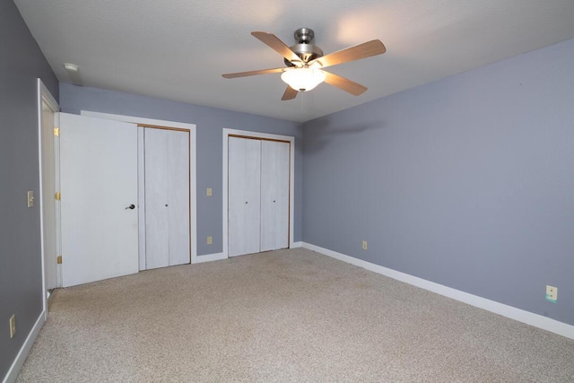 unfurnished bedroom with baseboards, multiple closets, carpet, and ceiling fan