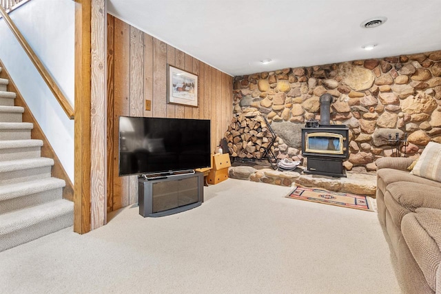 carpeted living room featuring stairs, visible vents, wood walls, and a wood stove