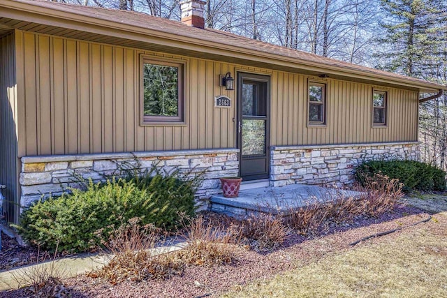 doorway to property with board and batten siding, stone siding, and a chimney