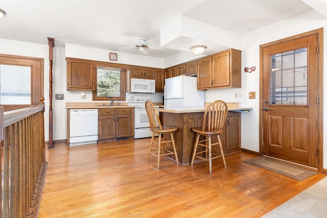 kitchen featuring white appliances, brown cabinetry, a peninsula, light wood-style flooring, and a sink