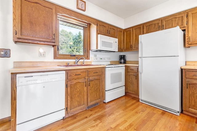 kitchen with light wood-type flooring, brown cabinets, a sink, white appliances, and light countertops