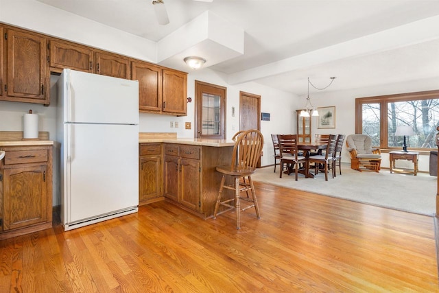 kitchen featuring light wood-type flooring, freestanding refrigerator, a peninsula, brown cabinetry, and light countertops