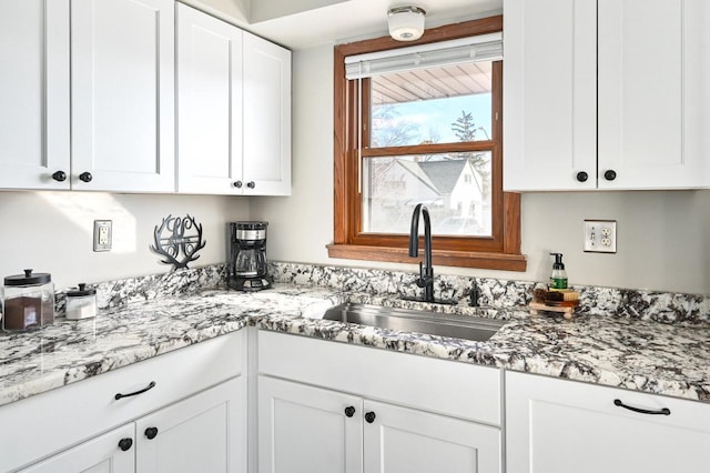 kitchen featuring a sink, light stone countertops, and white cabinetry