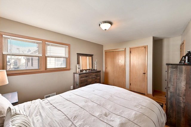 bedroom featuring wood finished floors, visible vents, and two closets