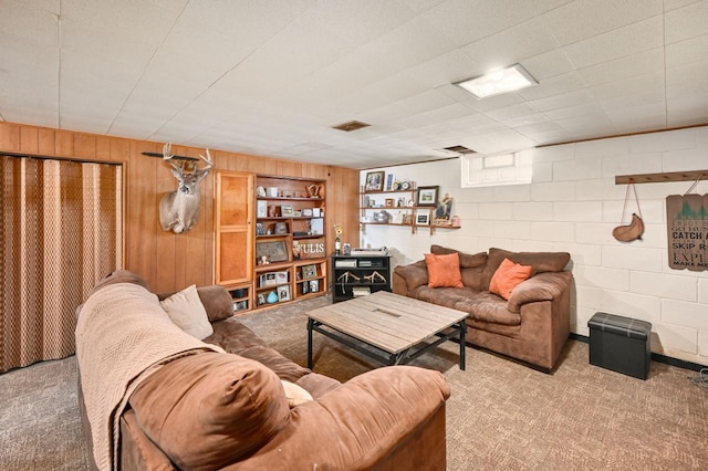 carpeted living area with visible vents, wood walls, and concrete block wall