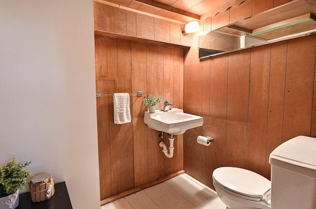 half bath with a sink, toilet, and wood walls