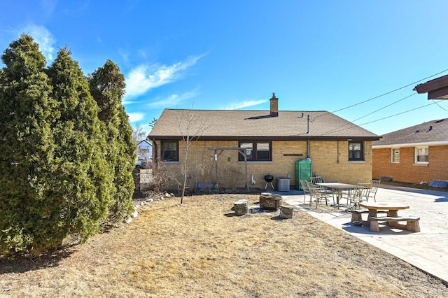 rear view of house with brick siding, a shingled roof, central air condition unit, a chimney, and a patio area