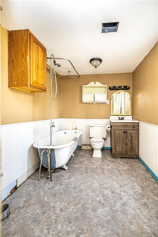 full bath with a soaking tub, toilet, and a wainscoted wall