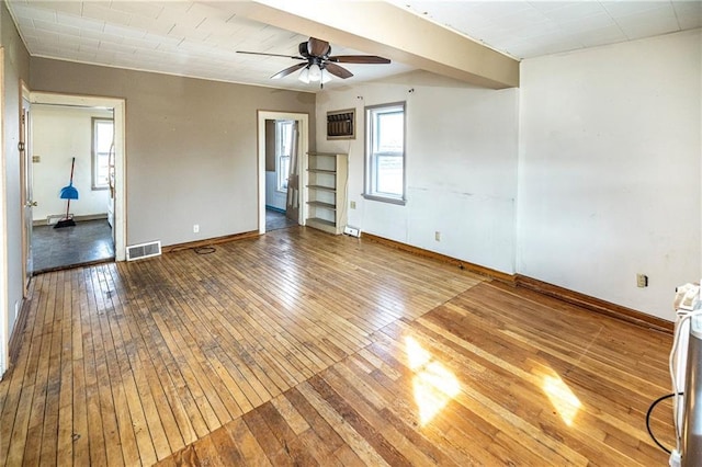 empty room with visible vents, a ceiling fan, baseboards, and wood-type flooring