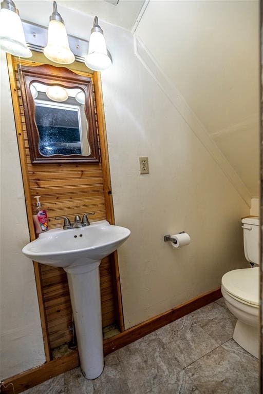 half bath featuring toilet, baseboards, and a sink