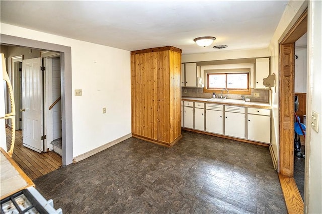 kitchen with baseboards, a sink, light countertops, white cabinets, and dark floors