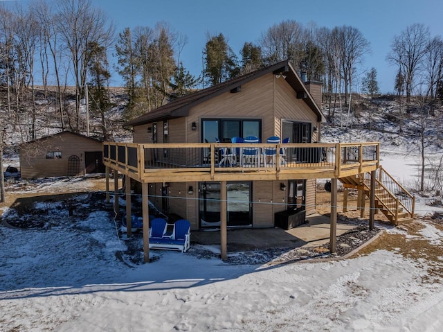 snow covered back of property featuring a chimney, stairway, a wooden deck, and a patio