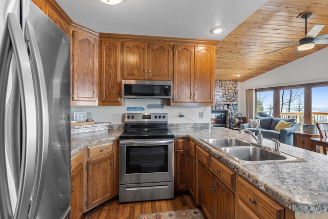 kitchen with a sink, dark wood finished floors, appliances with stainless steel finishes, a peninsula, and brown cabinetry