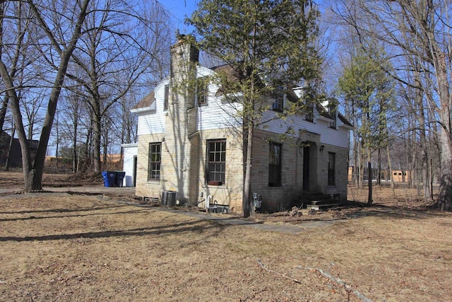 view of property exterior with entry steps, central AC unit, brick siding, and a chimney