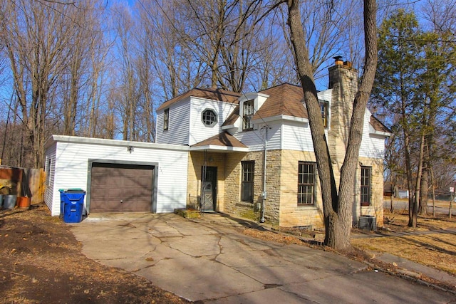 view of front of house with central air condition unit, driveway, stone siding, roof with shingles, and an attached garage