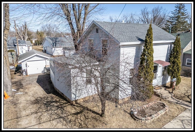 exterior space featuring a detached garage, an outbuilding, roof with shingles, and driveway