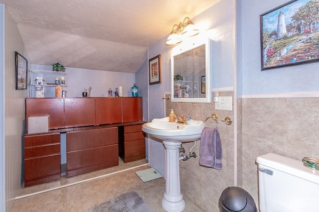 bathroom with tile walls, toilet, lofted ceiling, wainscoting, and a textured ceiling