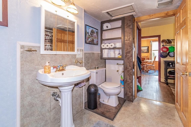 bathroom featuring visible vents, toilet, tile walls, and wainscoting