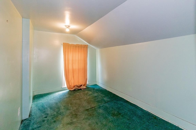 additional living space featuring dark carpet, baseboards, and vaulted ceiling