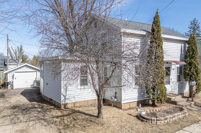 view of side of property with a detached garage, an outdoor structure, dirt driveway, and a shingled roof