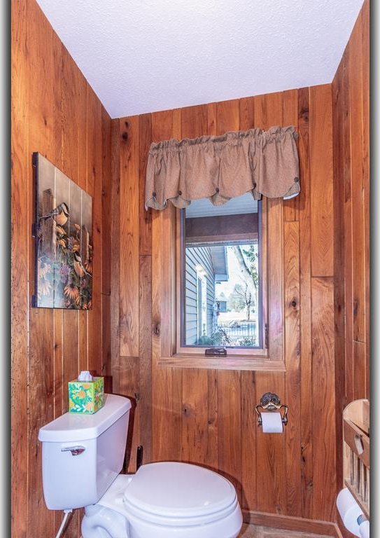 half bath featuring wood walls, a textured ceiling, and toilet