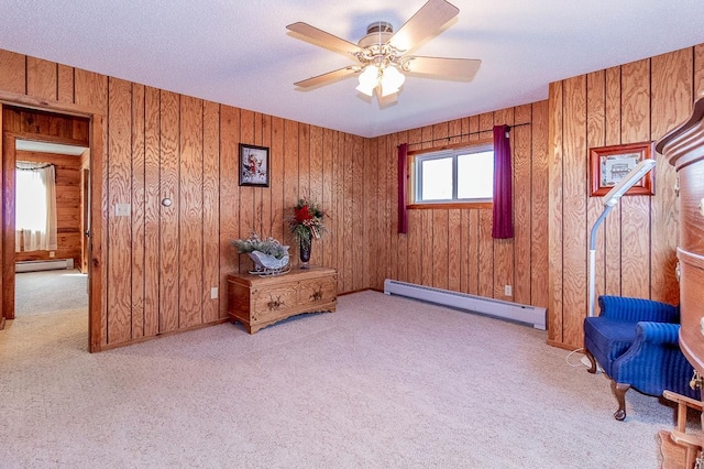 sitting room with wooden walls, a baseboard radiator, ceiling fan, carpet flooring, and baseboard heating