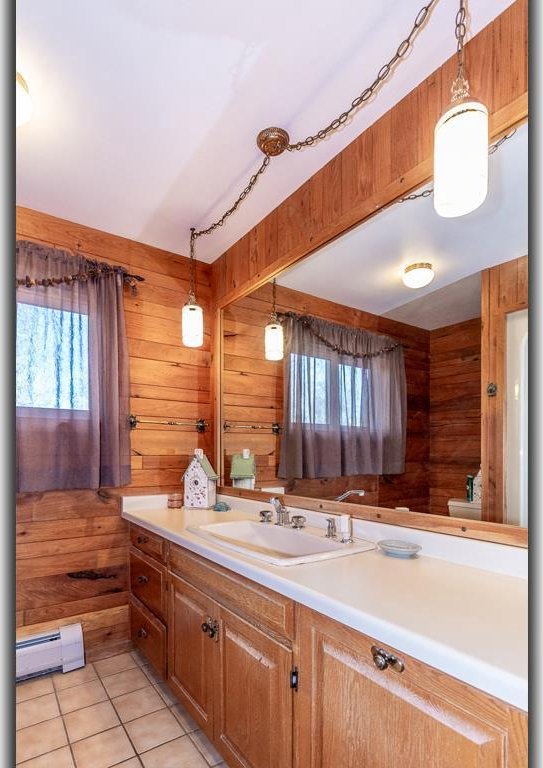 bathroom with a baseboard heating unit, wooden walls, vanity, and tile patterned flooring