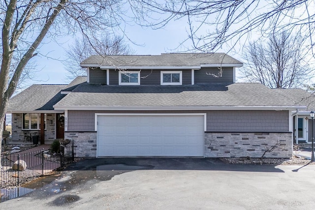 view of front of property with aphalt driveway, stone siding, fence, a shingled roof, and a garage