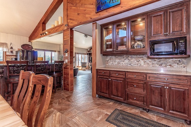 interior space featuring lofted ceiling, freestanding refrigerator, stone finish floor, black microwave, and tasteful backsplash