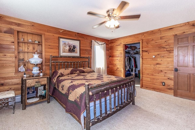 carpeted bedroom featuring a spacious closet, wood walls, a closet, a textured ceiling, and a ceiling fan