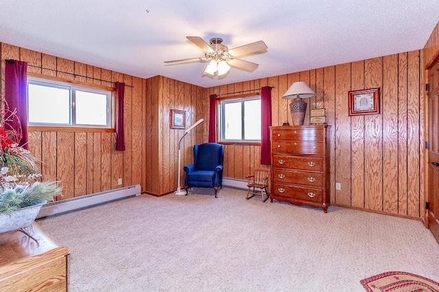 living area featuring a baseboard heating unit, wooden walls, carpet flooring, and a ceiling fan