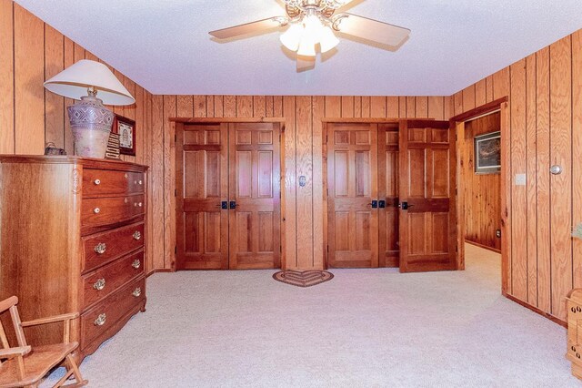 bedroom featuring wooden walls, a ceiling fan, carpet, and multiple closets