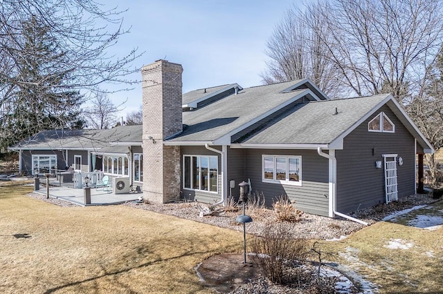 back of property with a shingled roof, a patio, a lawn, and a chimney