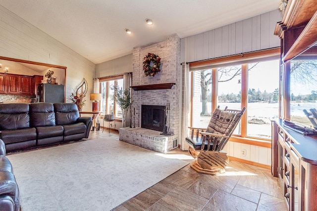 living area featuring lofted ceiling, a brick fireplace, wooden walls, and a healthy amount of sunlight