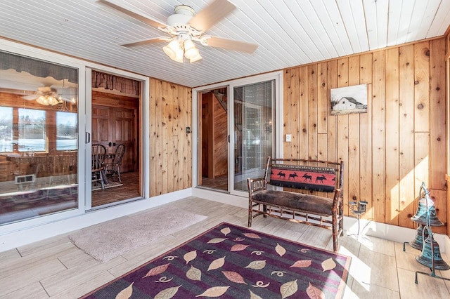 sitting room with a ceiling fan, wood finished floors, wood walls, a sunroom, and wood ceiling