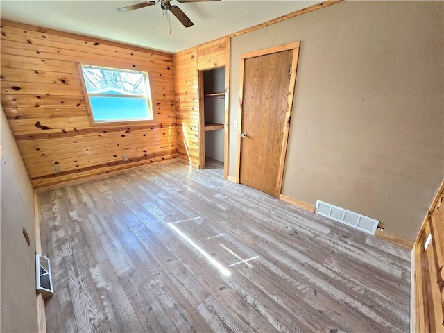 unfurnished bedroom featuring visible vents, wood walls, two closets, and hardwood / wood-style flooring