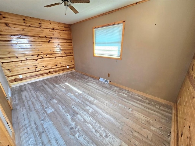 unfurnished room featuring visible vents, baseboards, wood walls, a ceiling fan, and wood-type flooring