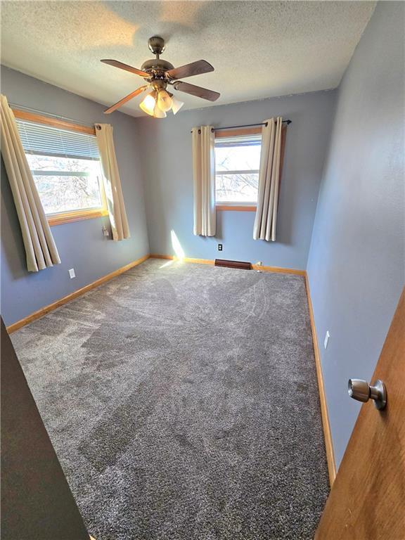 carpeted empty room with ceiling fan, a baseboard radiator, baseboards, and a textured ceiling