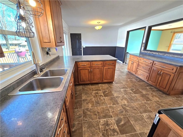 kitchen with a wainscoted wall, a peninsula, a sink, dark countertops, and brown cabinets