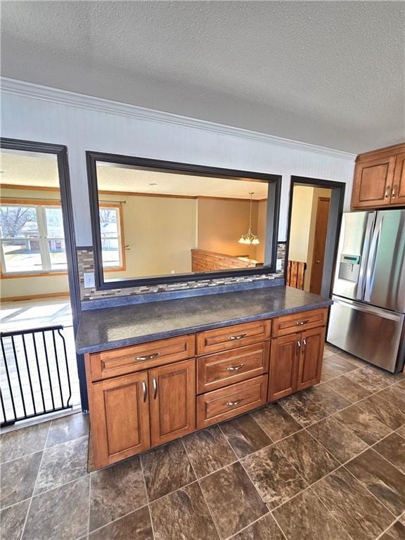 kitchen with dark countertops, brown cabinets, crown molding, and stainless steel fridge with ice dispenser