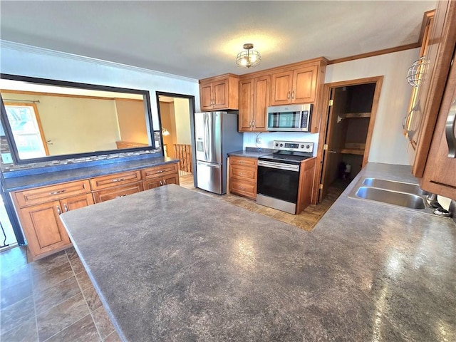 kitchen featuring dark countertops, ornamental molding, appliances with stainless steel finishes, a peninsula, and a sink