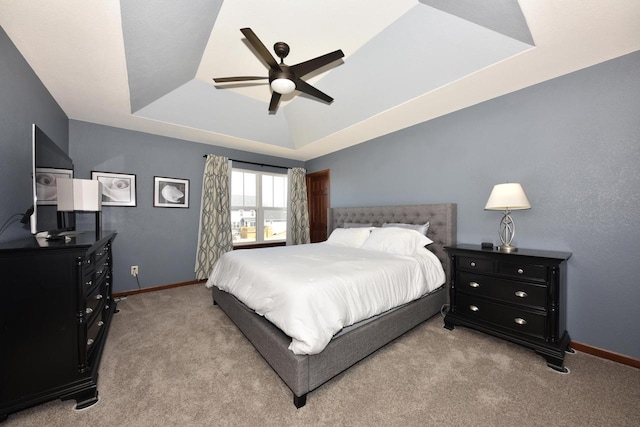 bedroom featuring light colored carpet, baseboards, a tray ceiling, and ceiling fan