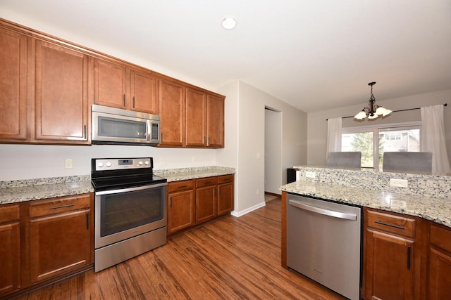 kitchen featuring light stone counters, dark wood-style flooring, stainless steel appliances, pendant lighting, and brown cabinets