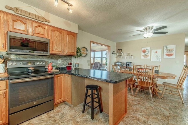 kitchen with dark countertops, a peninsula, stainless steel appliances, a kitchen breakfast bar, and a textured ceiling