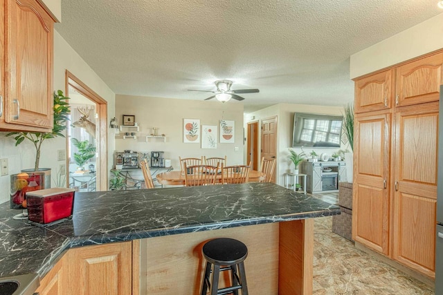 kitchen featuring a textured ceiling, a peninsula, a breakfast bar, and ceiling fan