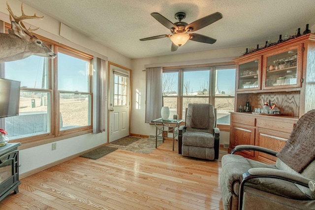 living area featuring baseboards, light wood-style floors, ceiling fan, and a textured ceiling