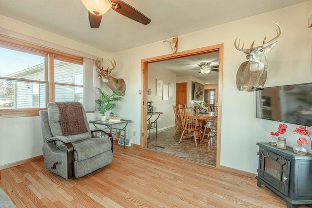 living area featuring a wood stove, a ceiling fan, baseboards, and light wood finished floors