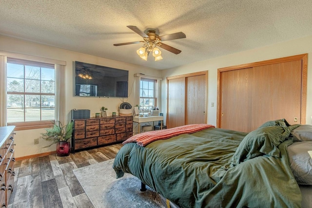 bedroom featuring wood finished floors, baseboards, ceiling fan, multiple closets, and a textured ceiling