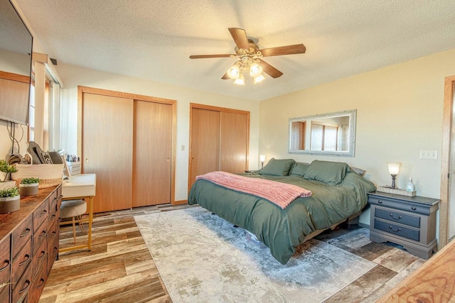 bedroom featuring light wood-style floors, two closets, a ceiling fan, and a textured ceiling